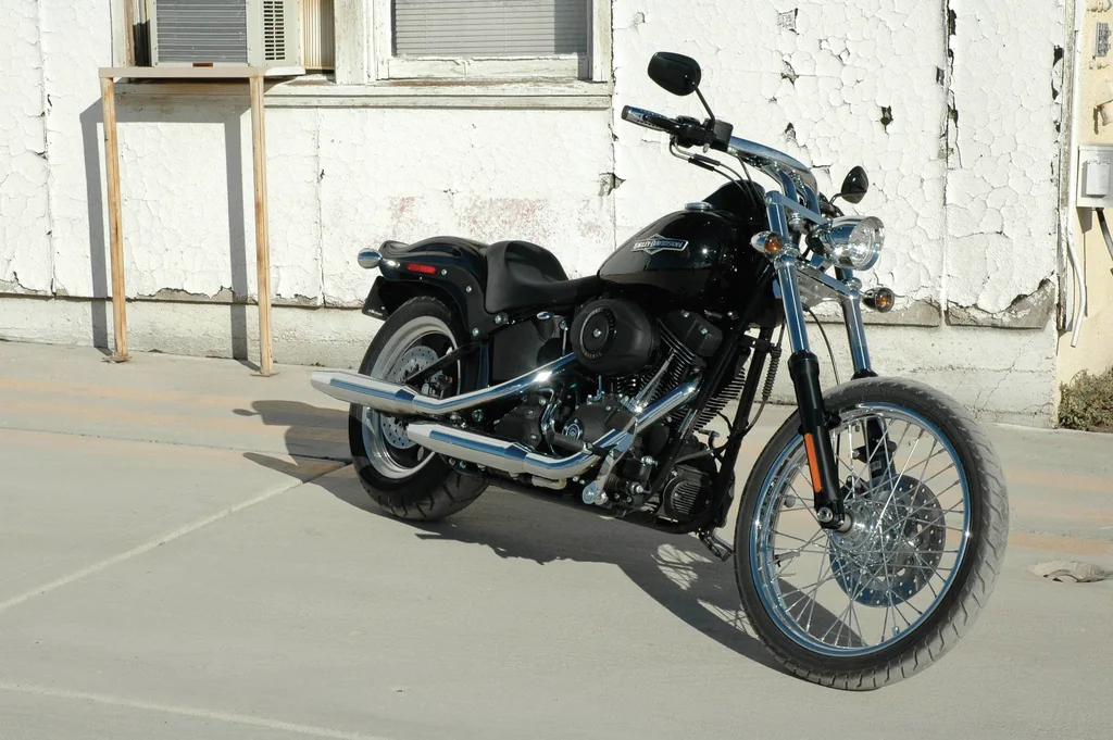 A black Harley-Davidson Night Train with a solo seat, narrow wire-spoked front wheel and chrome exhaust, parked outside a building.