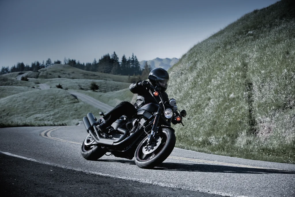 A rider on a black Harley-Davidson XR1200X leaning through a bend on a hillside road.